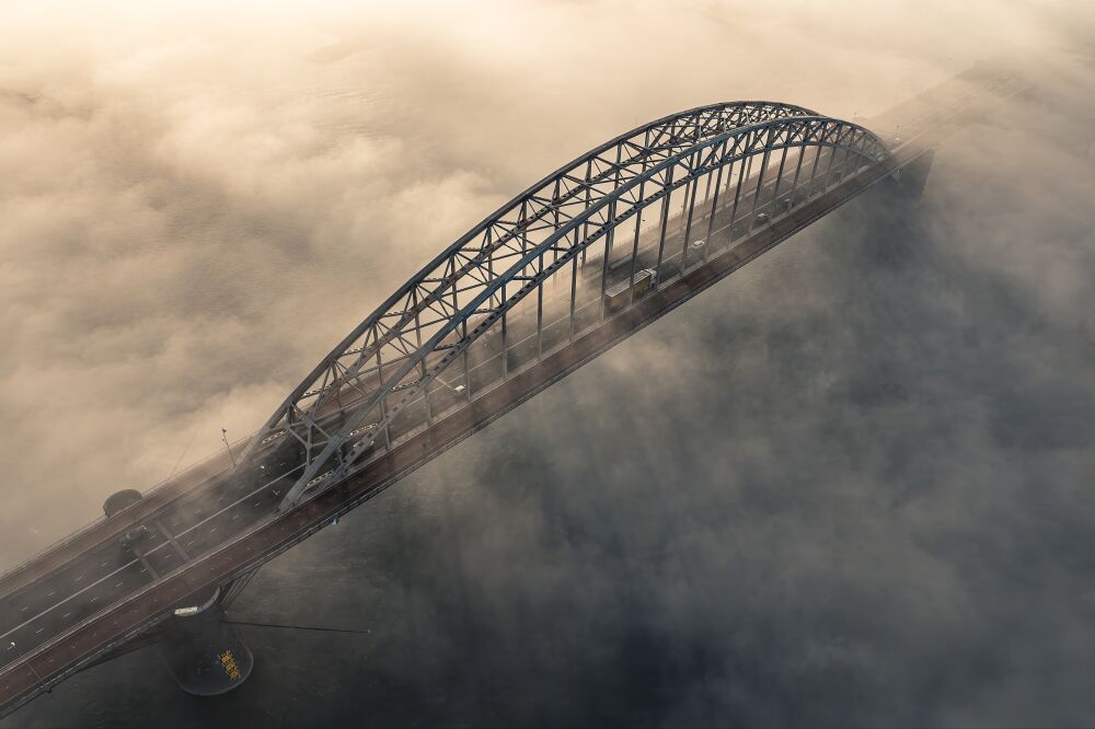 Forenzen op de Waalbrug boven de mist bij zonsopkomst