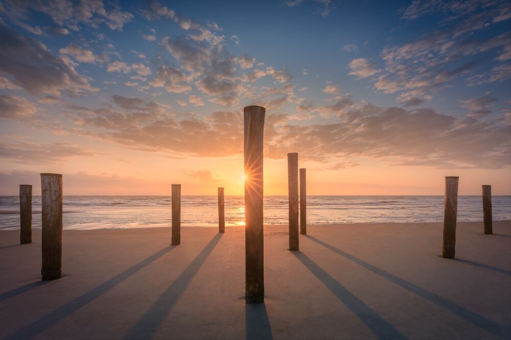 Zonsondergang door houten palen op het strand