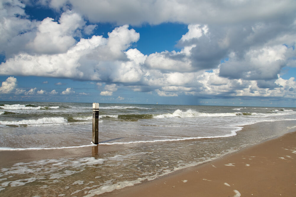 Strand met paal en mooie Nederlandse wolkenlucht