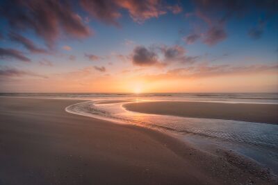 Zonsondergang aan de rustige kust met kronkelende getijdenstroom