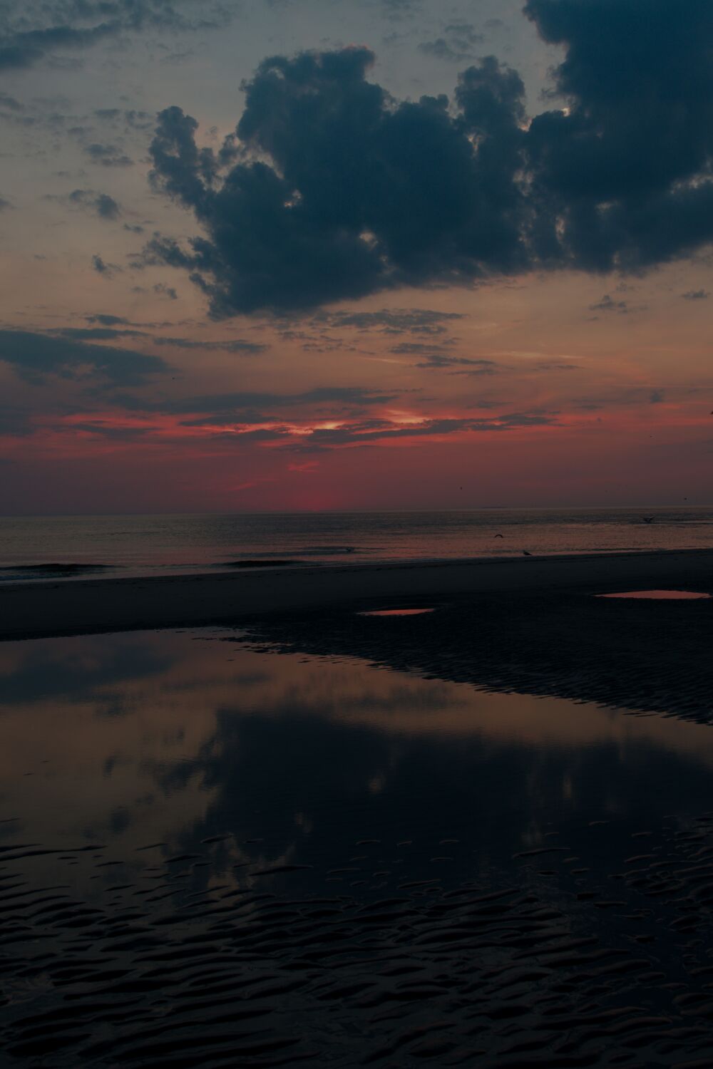 Weerspiegeling van de wolken bij zonsondergang aan het strand op Texel