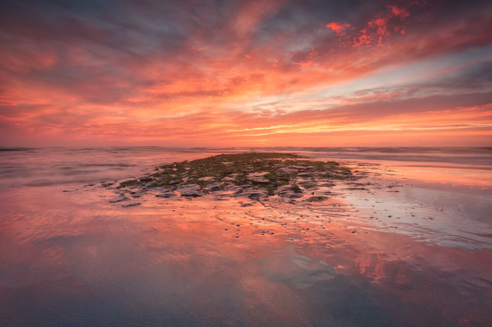 Vurige zonsondergang weerspiegeld op een kustlandschap