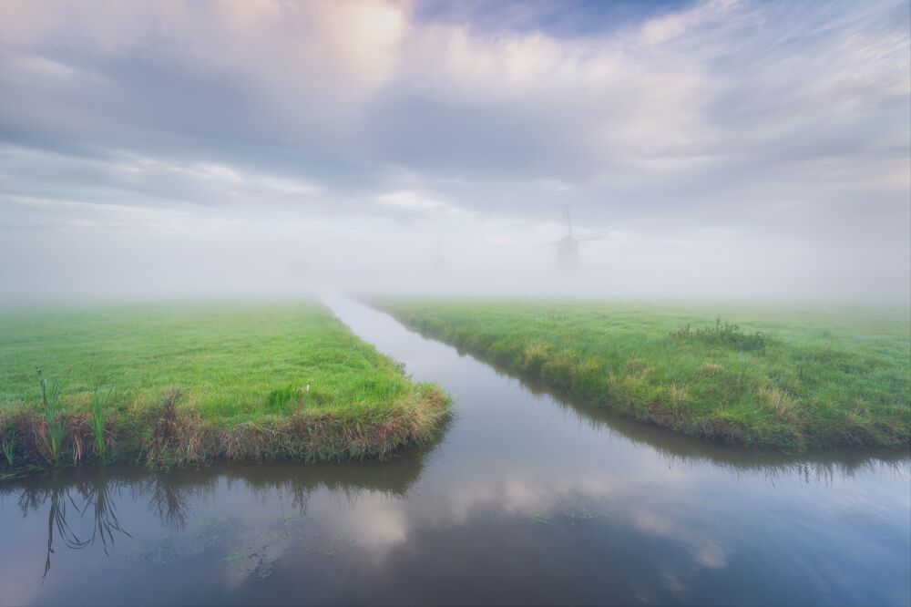 Hollands polderlandschap met molens tijdens een mistige zonsopkomst