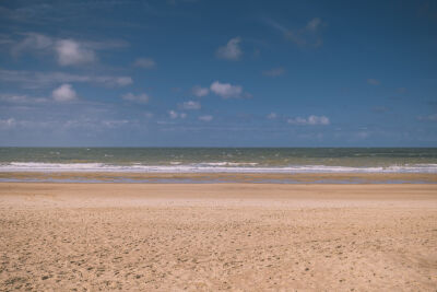 Zeezicht, zand op het strand en blauwe lucht met kleine wolken