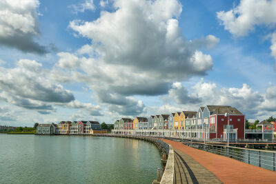 Gekleurde huizen aan de Rietplas aan de loopbrug, blauwe lucht met wolken