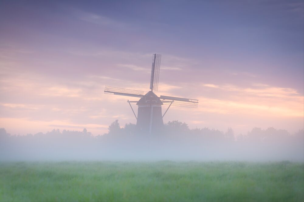 Hollands polderlandschap met molens tijdens een mistige zonsopkomst